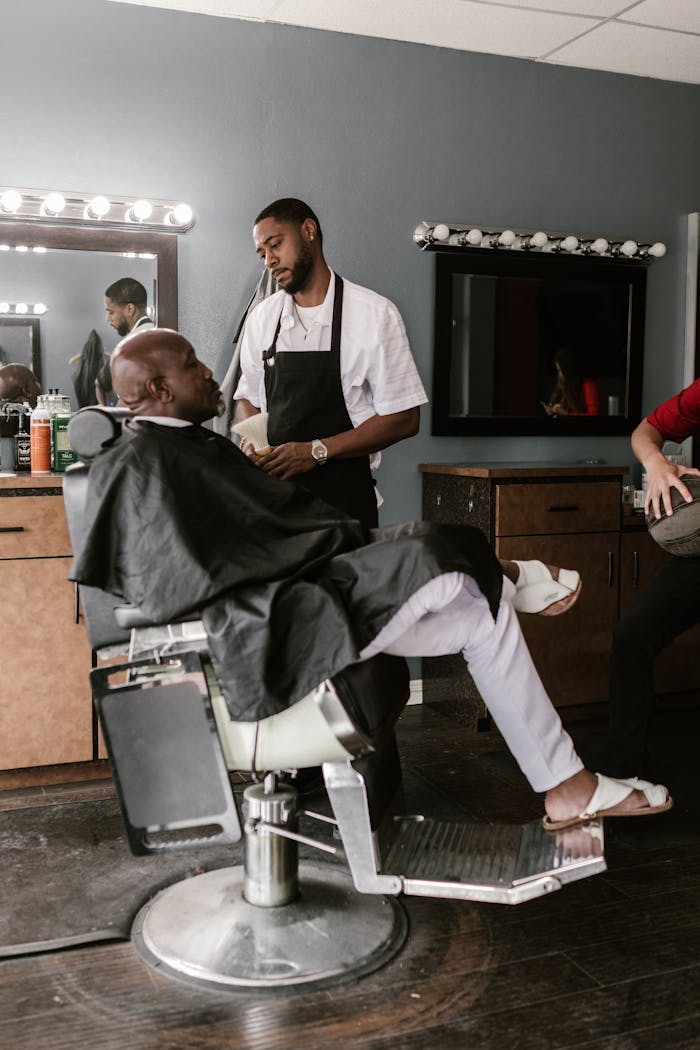 About Barber giving an African American man a haircut in a classic barbershop setting.