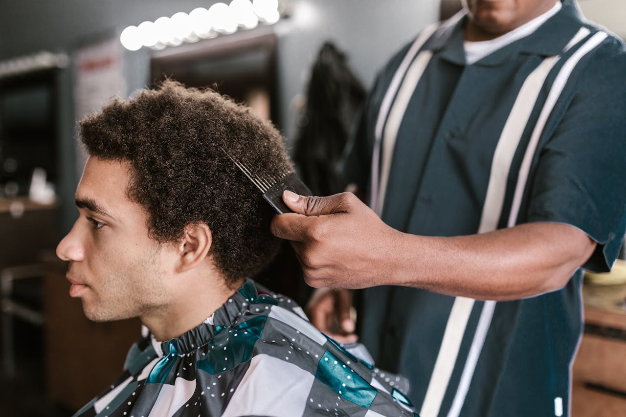 Services A barber uses an afro pick to style a client's hair in a modern barbershop setting.